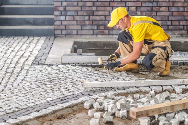 Professional Caucasian Worker Building Granite Paved Hardstanding Garden Path. Industrial Theme.